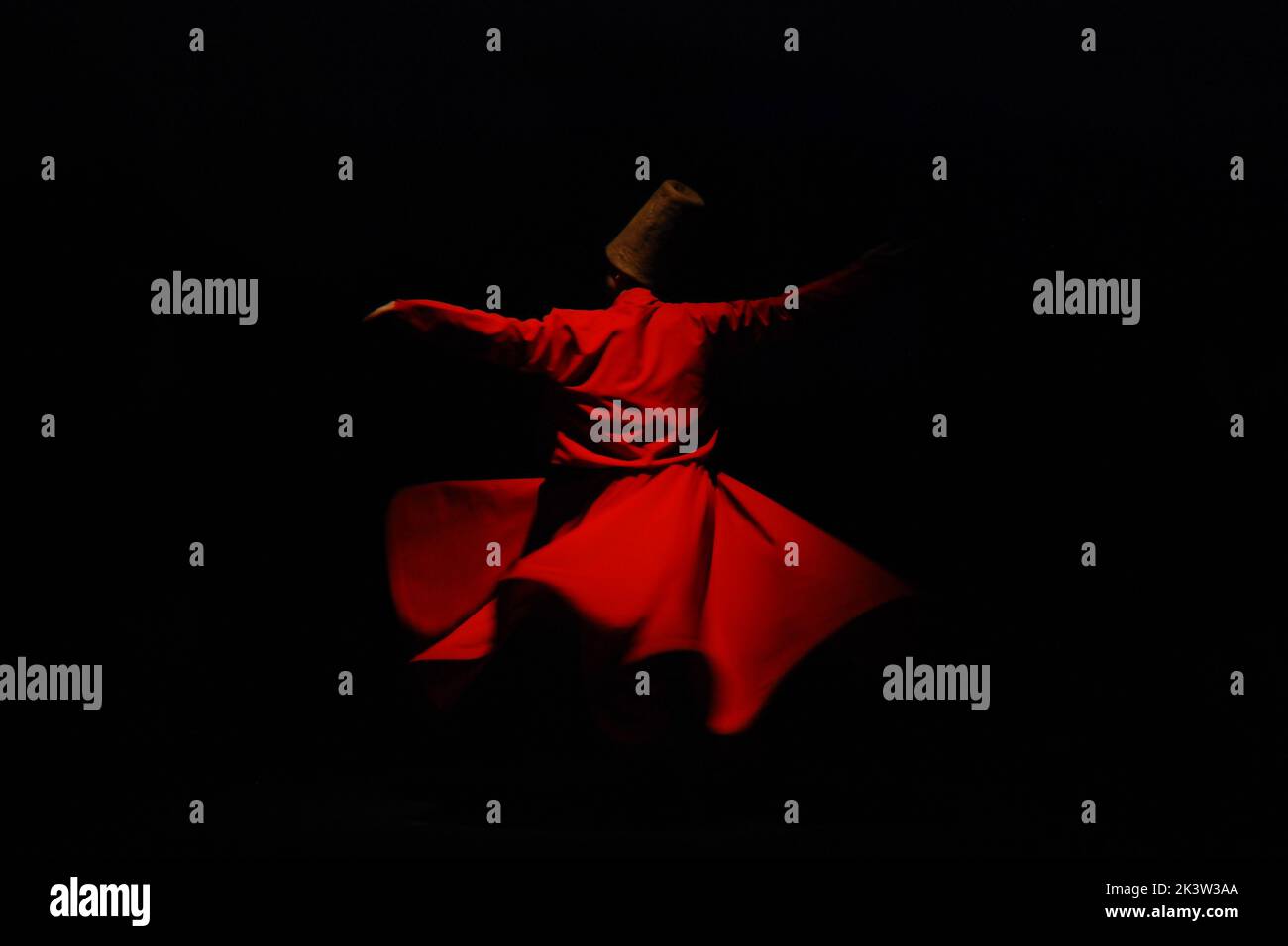 A person in a red dervish costume spinning on a black background Stock Photo