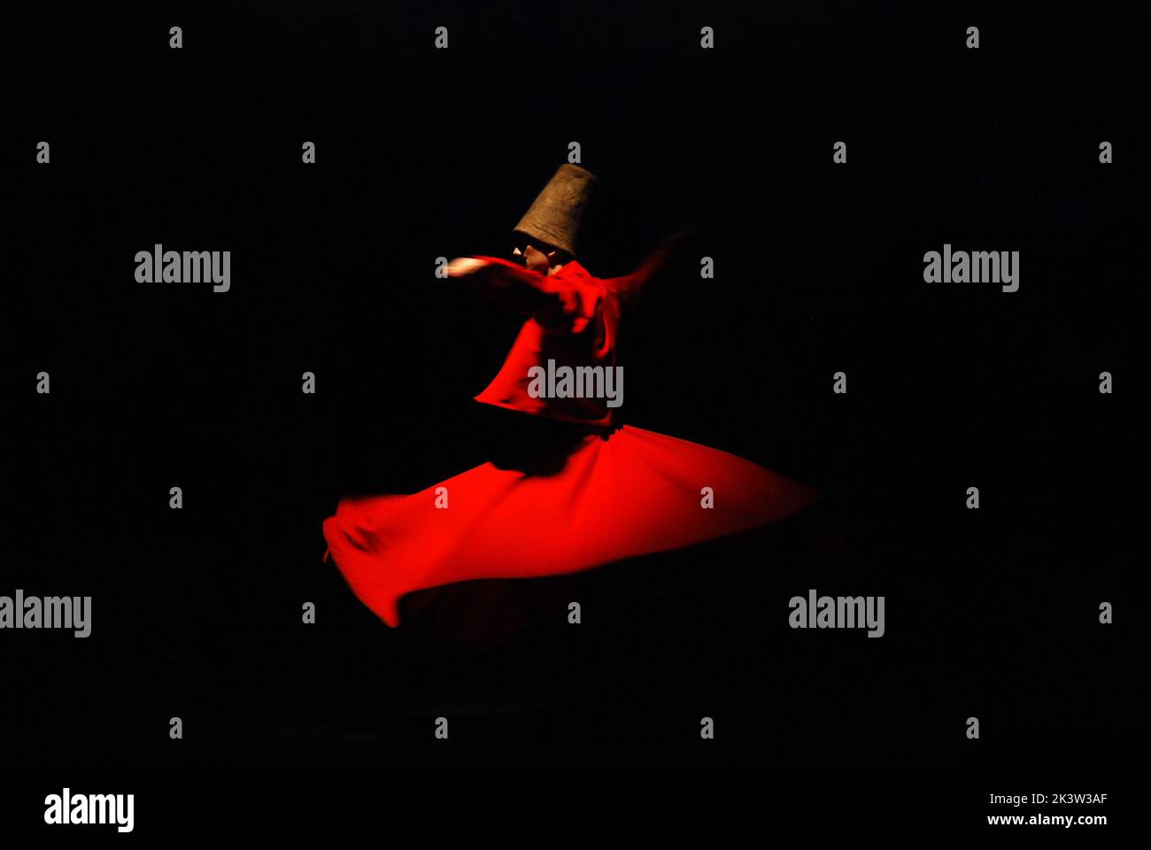 A person in a red dervish costume spinning on a black background Stock Photo