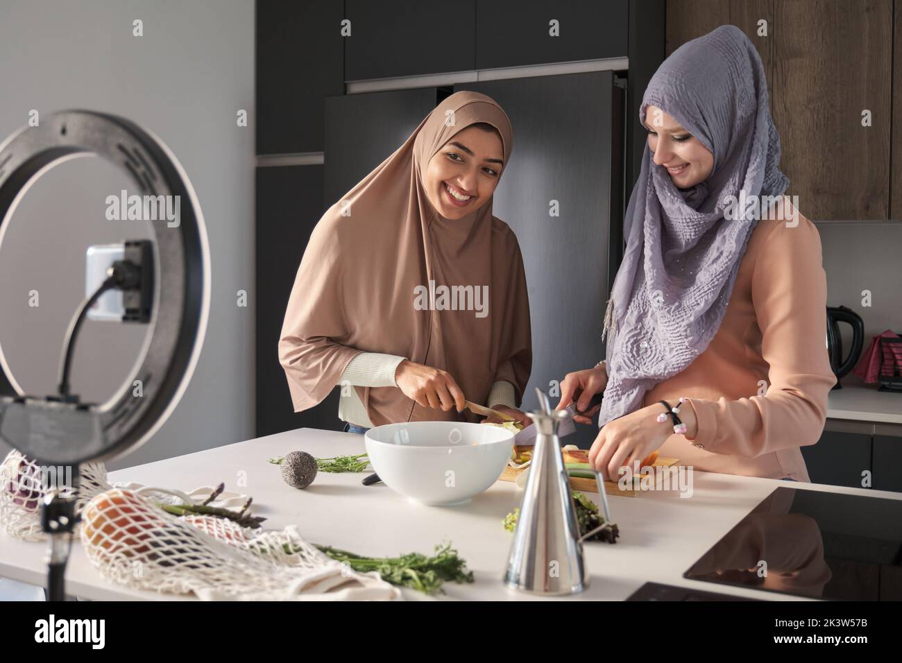 Two muslim food vloggers explaning how to prepare a salad at kitchen. Stock Photo