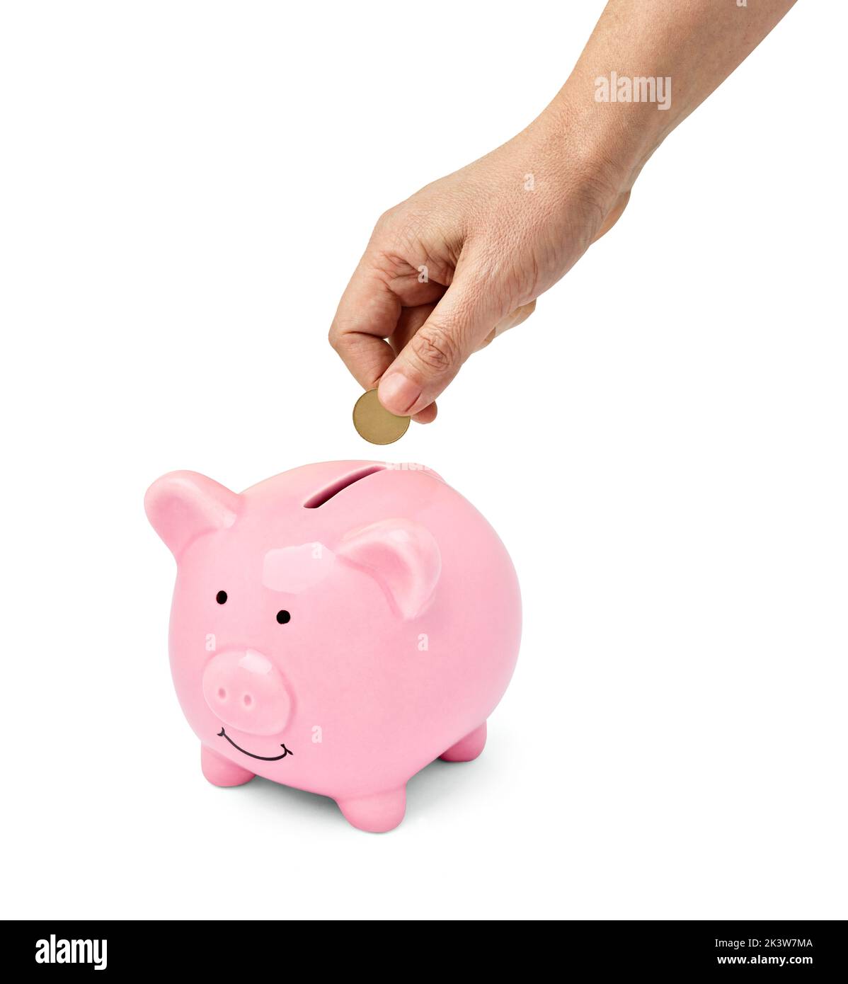 Close up of a hand holding a coin and putting in a pink piggy bank on white background Stock Photo