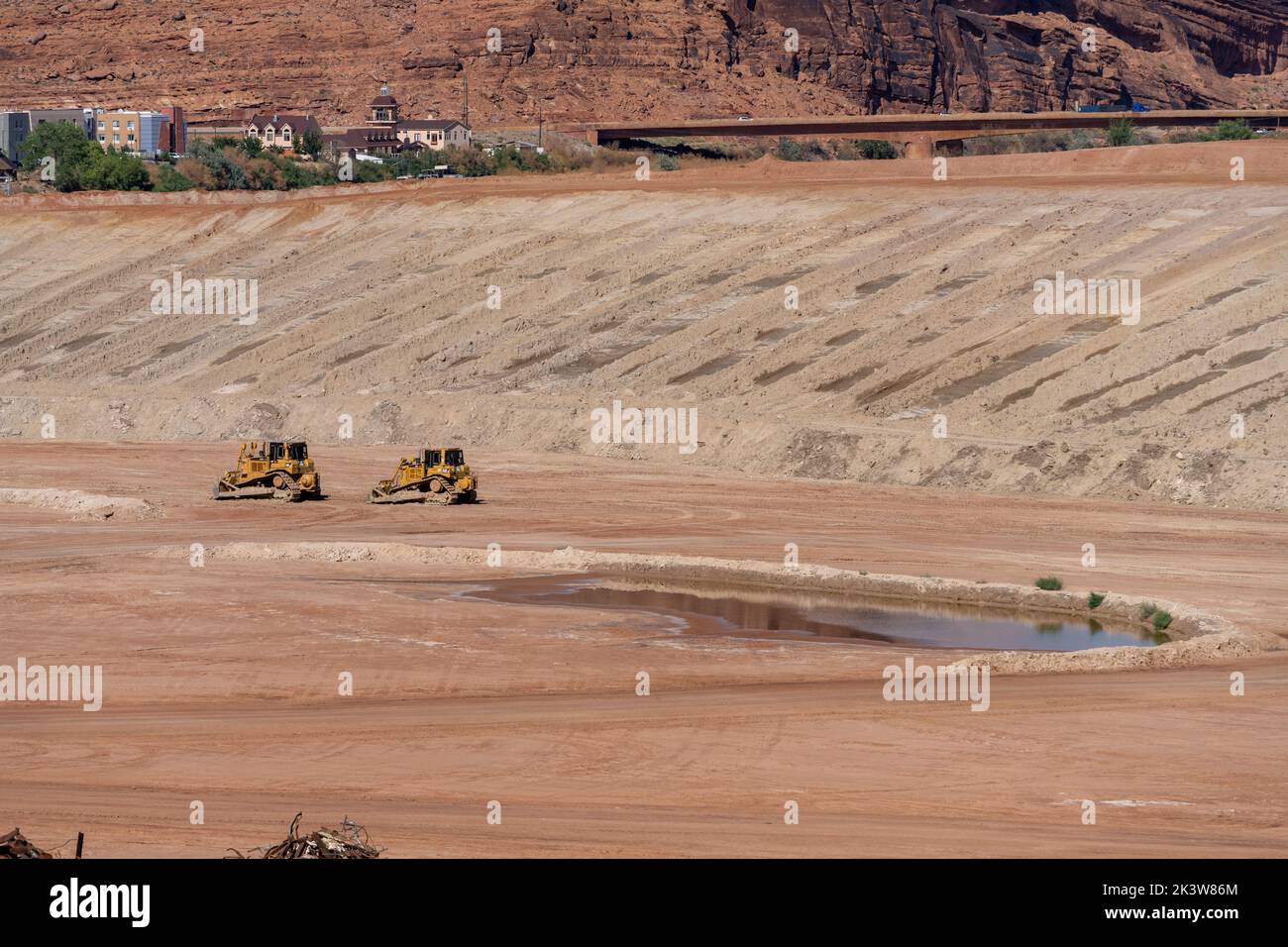 Heavy earth-moving equipment in the uranium tailings pile at the Moab UMPTRA Project.  Moab, Utah.  Nearby tourist hotels are in the background. Stock Photo