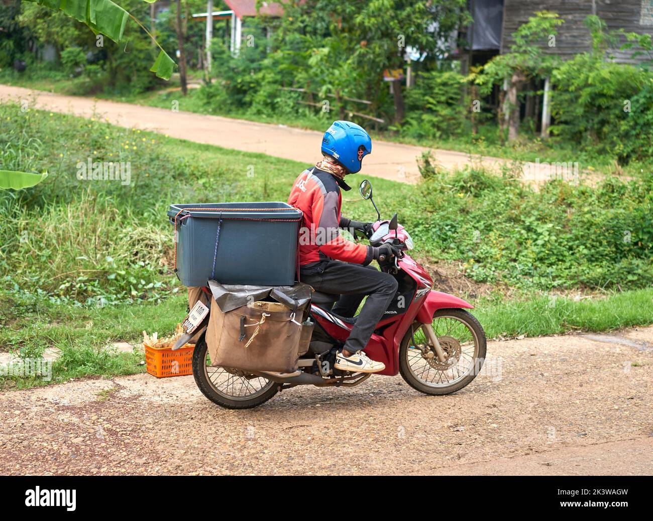 A motorcycle courier delivers packages in a rural area. Stock Photo