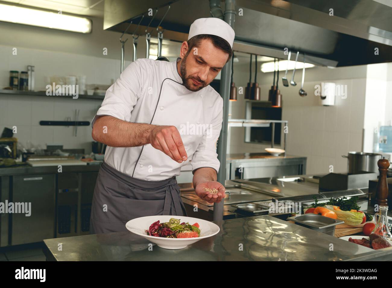 Chef sprinkles salt to salad of fresh vegetables in kitchen of restaurant. Tasty and healthy food Stock Photo