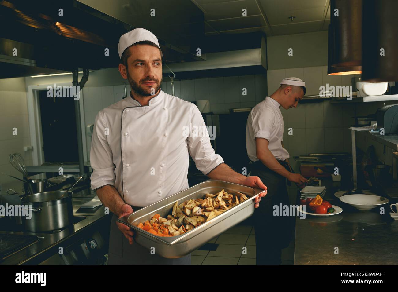 Chef holding tray with baked vegetables while standing in the kitchen of restaurant Stock Photo