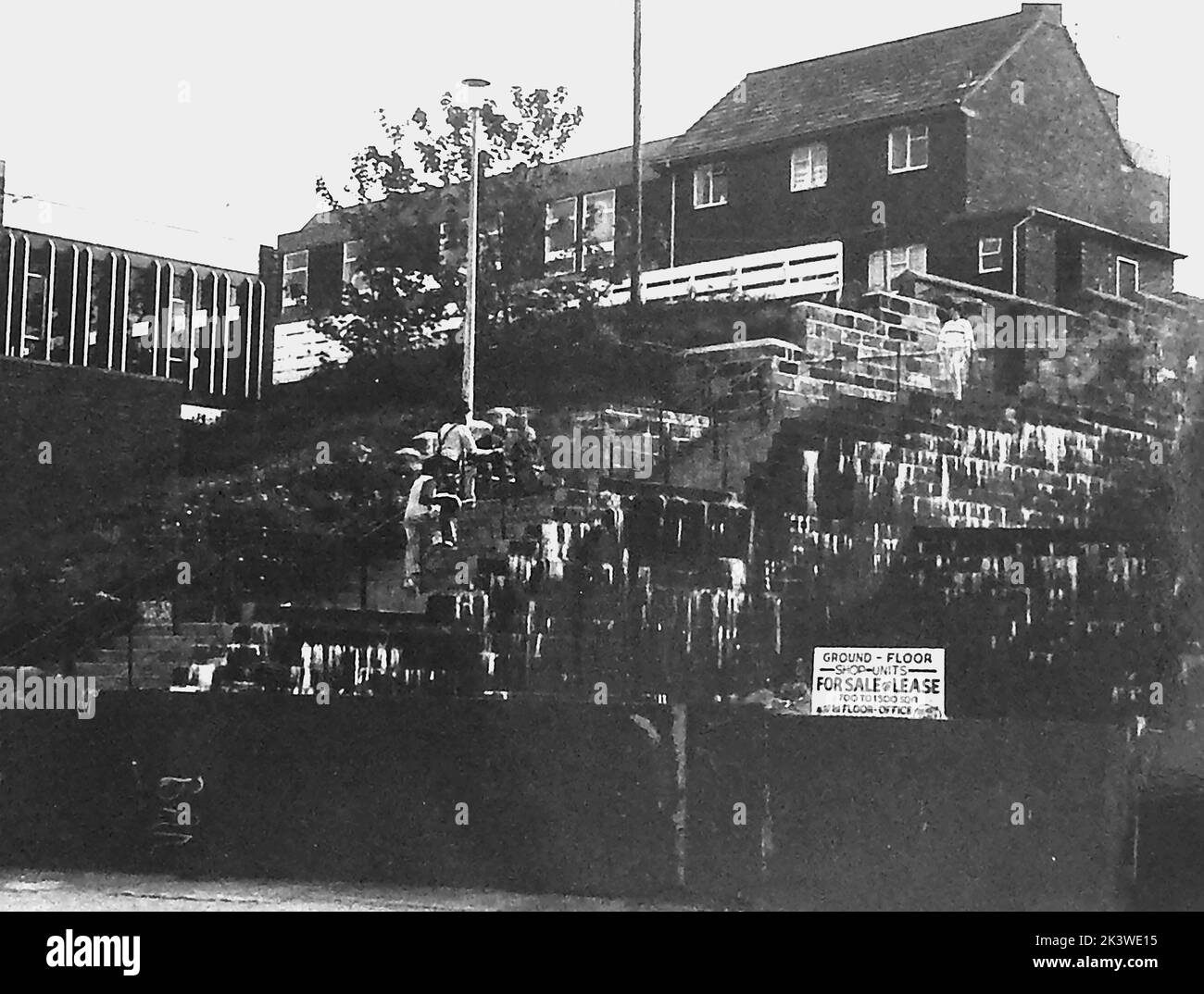 A vintage photograph of Bobby's Bank (aka Bobbies Bank)  before redevelopment at Whitby, Yorkshire, UK. The original bank  used by policemen was replaced by steps as seen in this picture. When redevelopment took place, shops were placed on the site and  another bank (the present one) with some steps replaced it. The modern building to the left is Whitby public library. Station Square is just out of shot to the right. Stock Photo