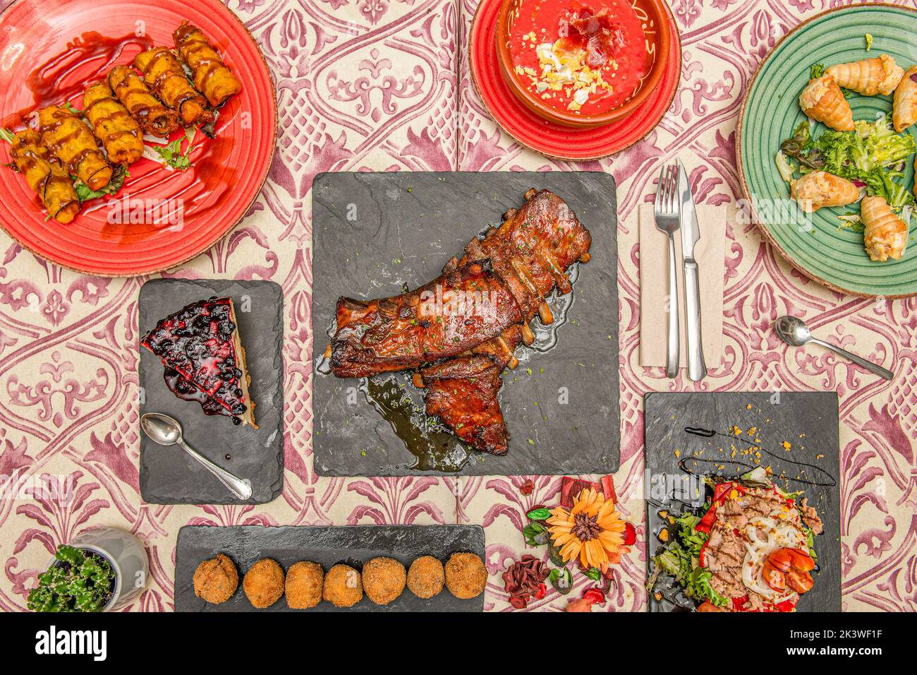 Several plates of food with croquettes, cones with salad, salmorejo, barbecue ribs, lemon cake and Russian salad with tomato and canned tuna Stock Photo