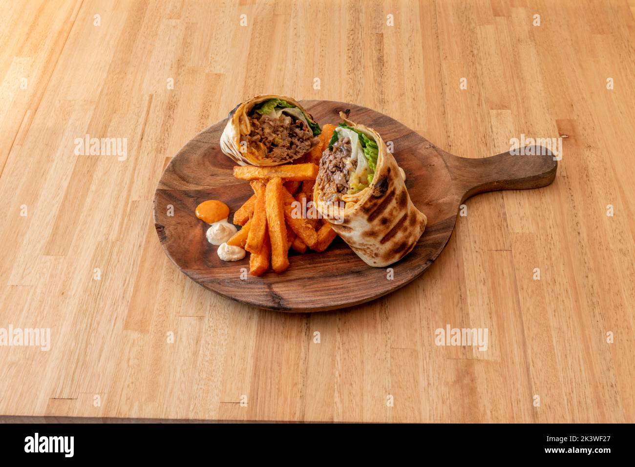 Wheat tortilla stuffed with lamb kebab with lettuce and fried sweet potatoes Stock Photo