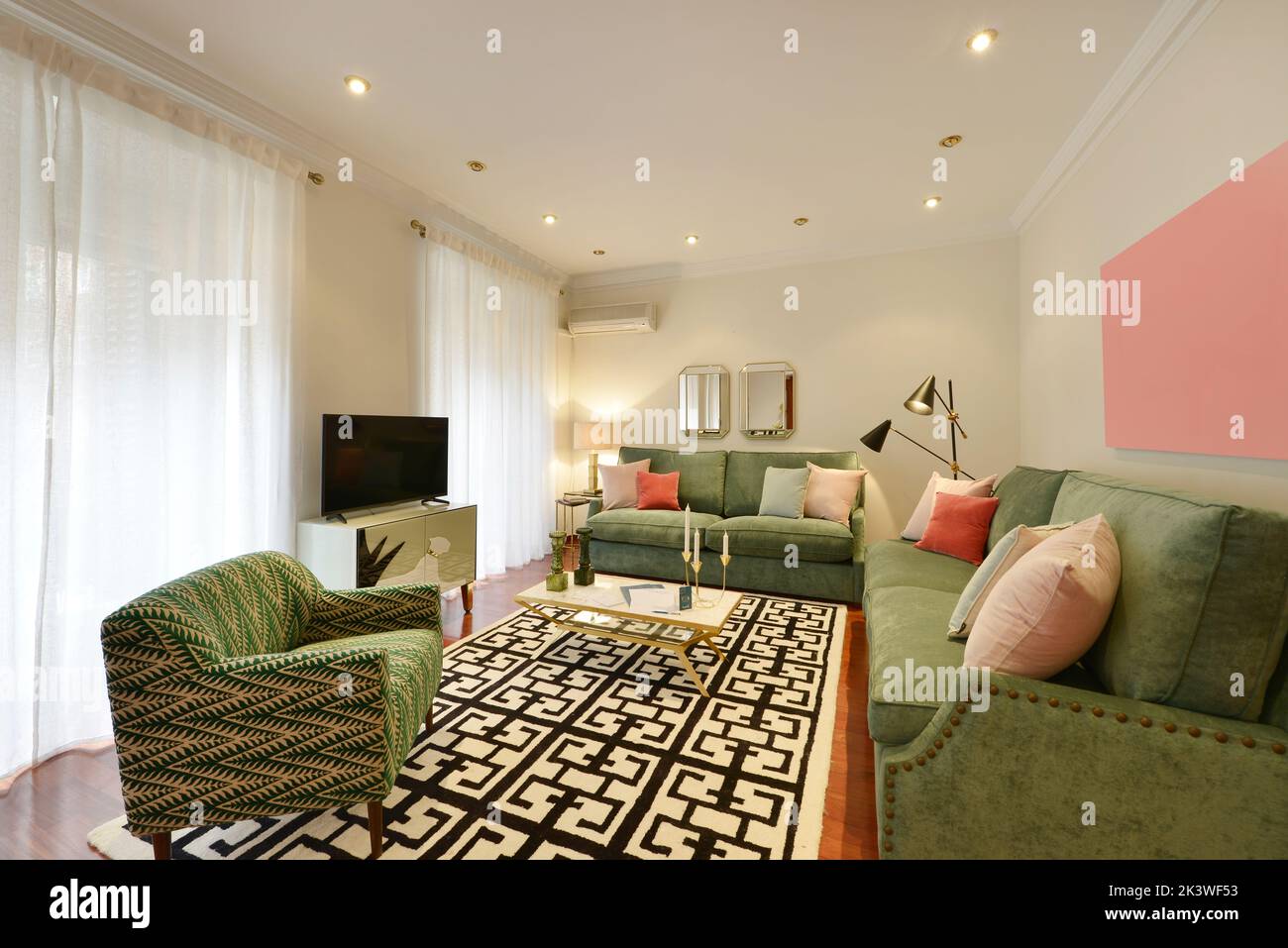 Living room of a house with one, two and three-seater sofas upholstered in green fabric with a wooden sideboard with a TV and balconies with curtains Stock Photo