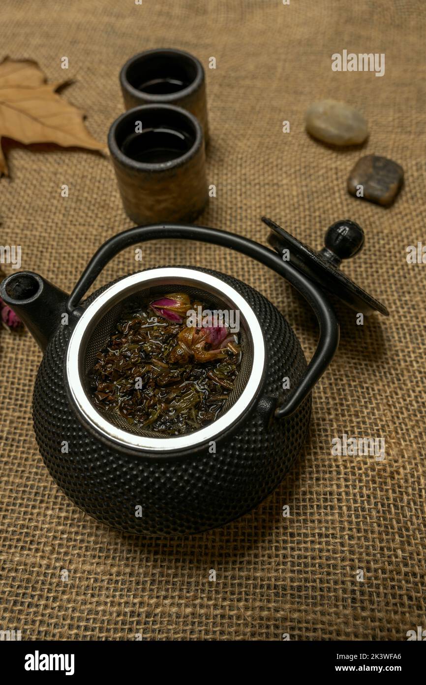 Autumn print with asian style black metal teapot with rose tea and green tea in the basket on burlap fabric Stock Photo
