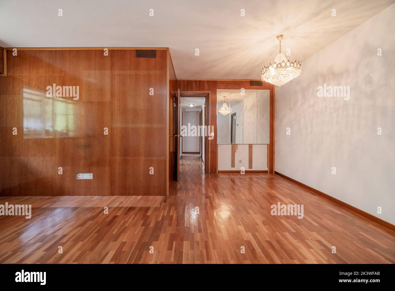 Empty room with varnished wood mural and mirrors, a crystal chandelier and matching parquet floors Stock Photo