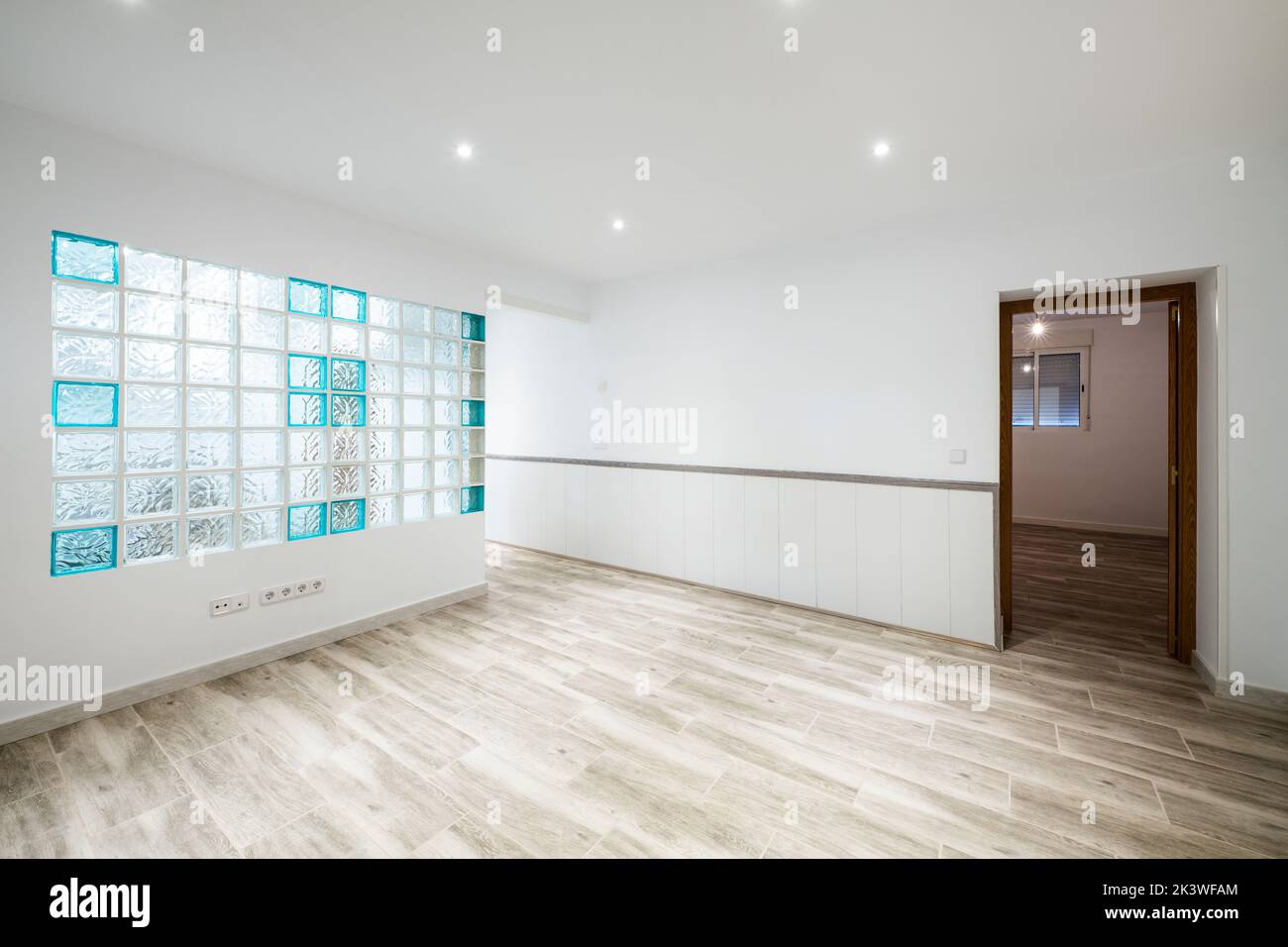 Empty living room with glass paving skylight on one wall and gray stoneware flooring and access to a room with a window Stock Photo