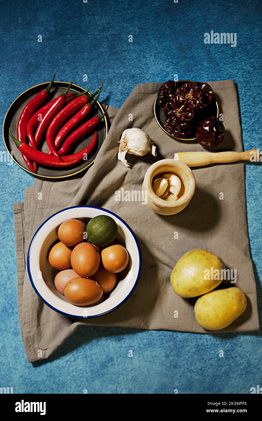 Still life with a bowl of raw eggs, raw potatoes, garlic in a wooden mortar, dried peppers and red hot peppers Stock Photo
