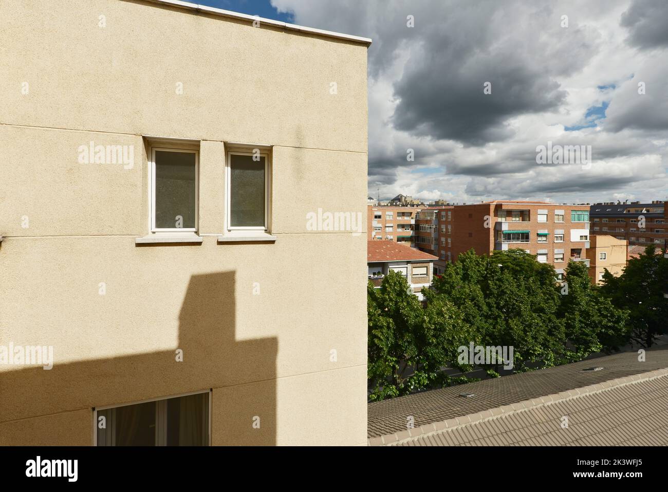 Facade of a house with a light wall, small white aluminum windows and rain-bearing clouds Stock Photo