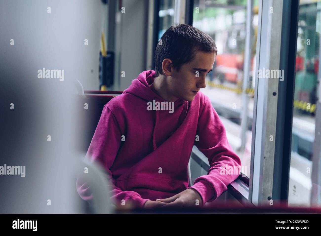 Teenage boy in a pink hooded sweatshirt, pensive s traveling by bus Stock Photo