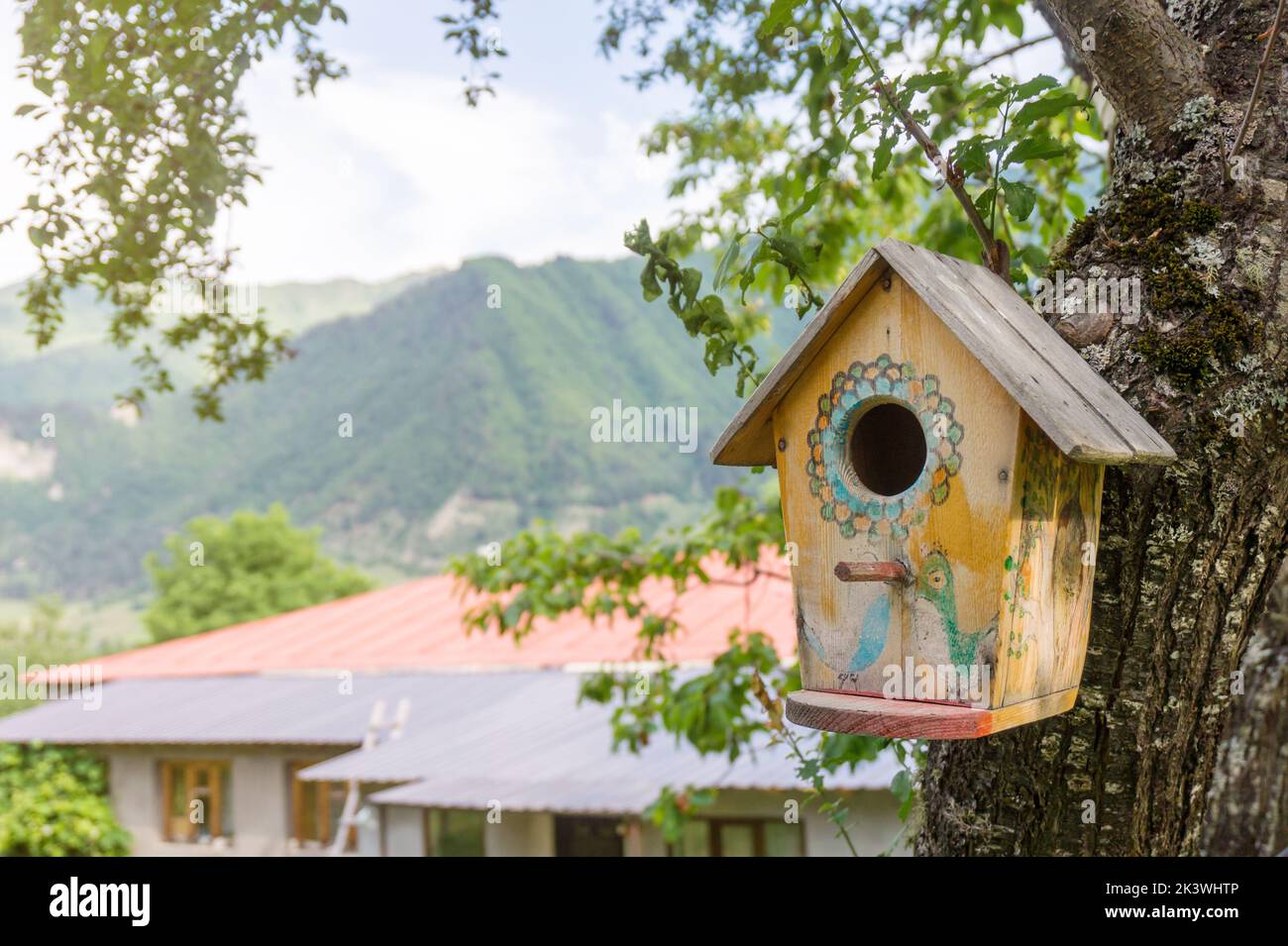 Wooden birdhouse on a tree in the garden. Little yellow cute decorated nesting box on a Summer day. Stock Photo