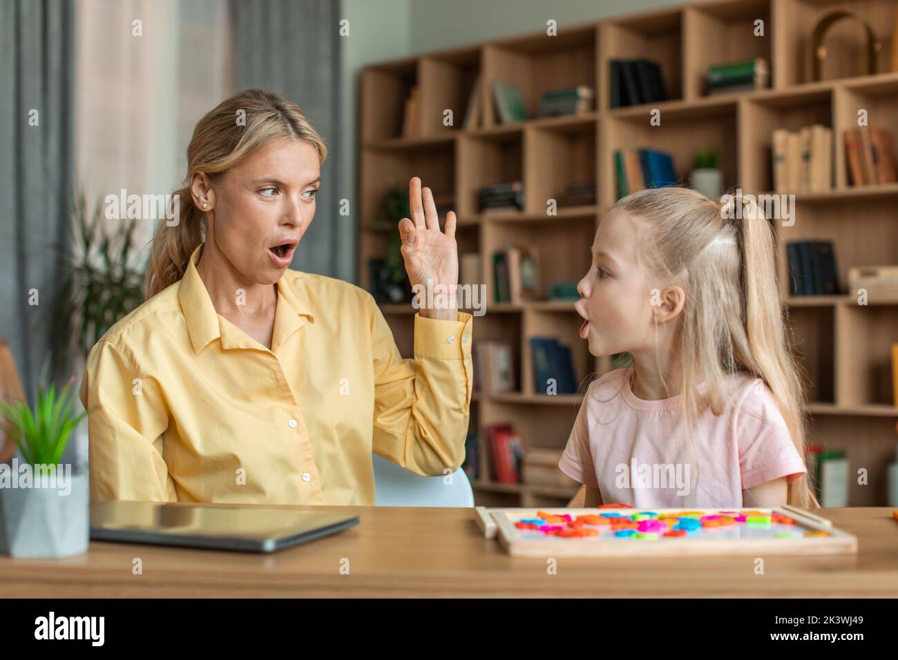 Professional female speech therapist studying together with little kid girl, learning practice pronunciation exercises Stock Photo