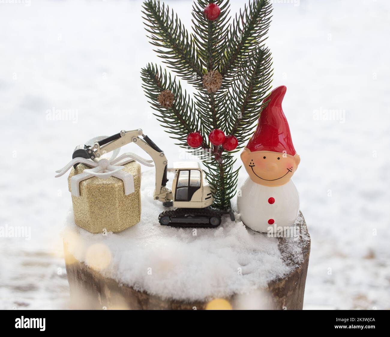 miniature toy construction excavator and souvenir figurine of elf,coniferous branch stand in snow in composition on theme of New Year, Christmas greet Stock Photo