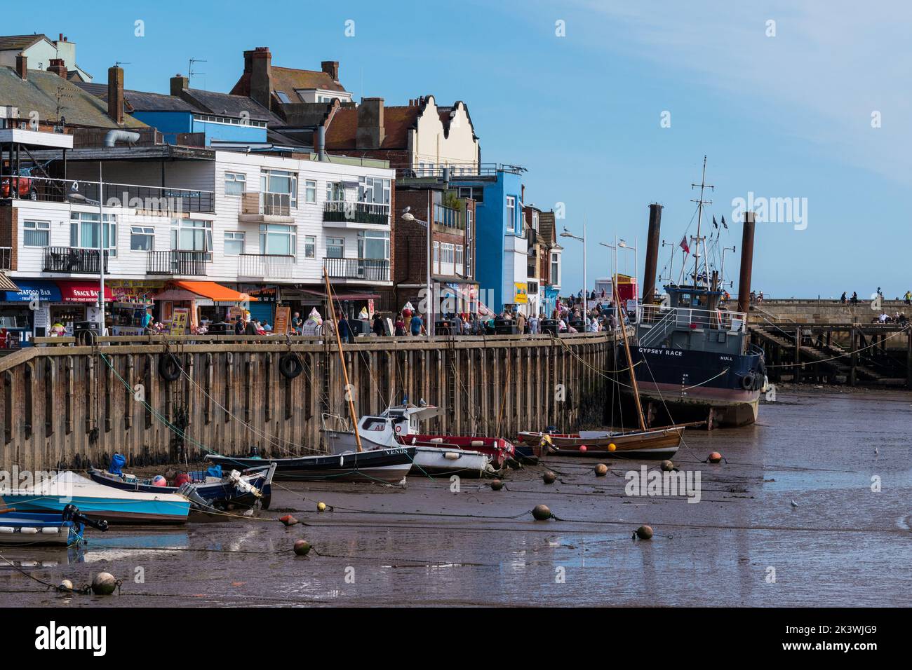 The commercial fishing harbour in Bridlington East Yorkshire, with small and larger fishing boats alongside the harbour wall and quayside shops. Stock Photo