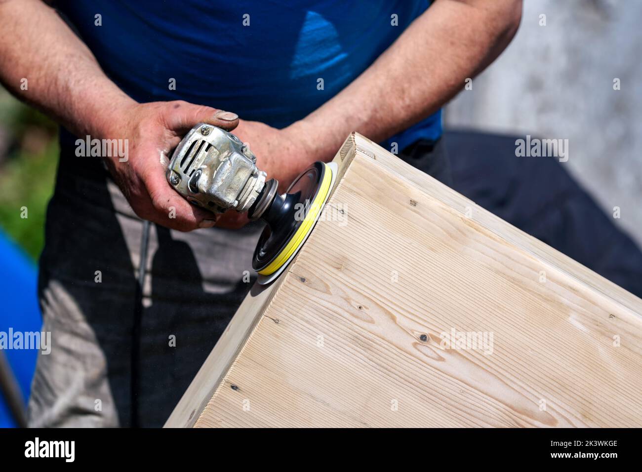Man polishing wooden chest with old angle grinder during sunny day, closeup detail to hands without gloves Stock Photo