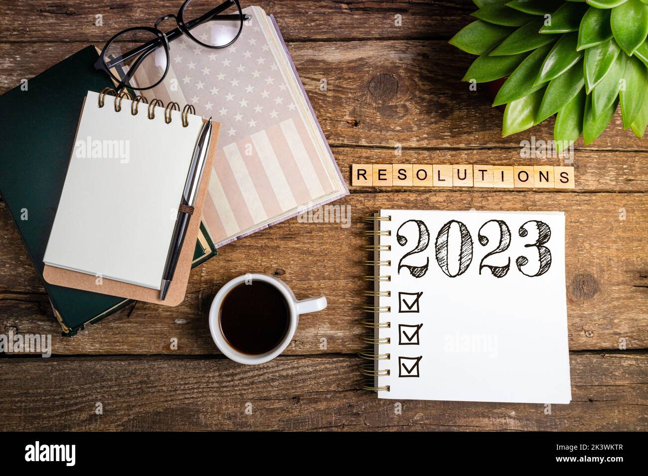 New year goals 2023 on desk. 2023 resolutions list with notebook, coffee cup and eyeglasses on