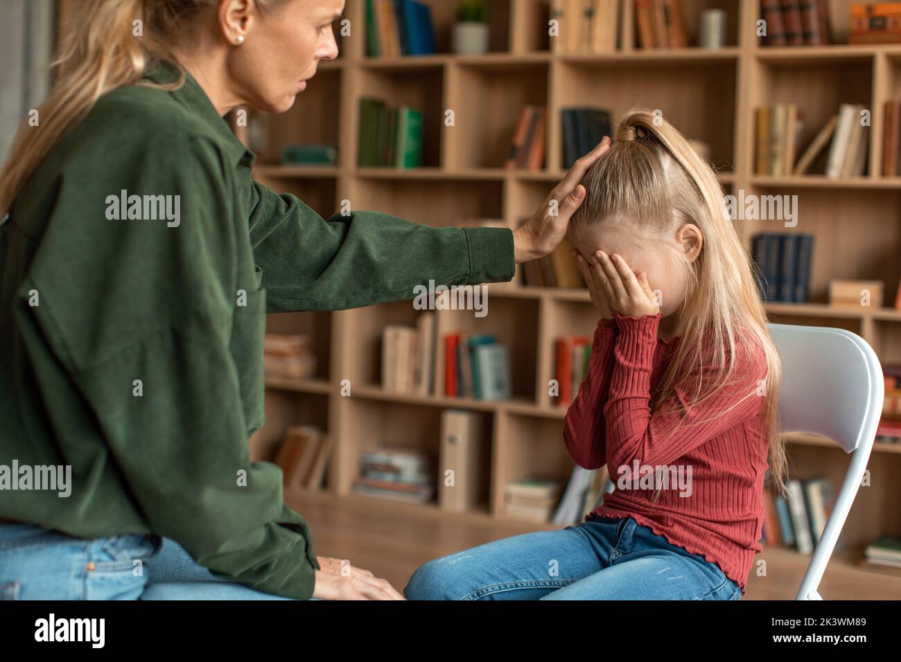 Little scared girl hiding face behind hands, ignoring caring female psychologist during personal consultation at office Stock Photo