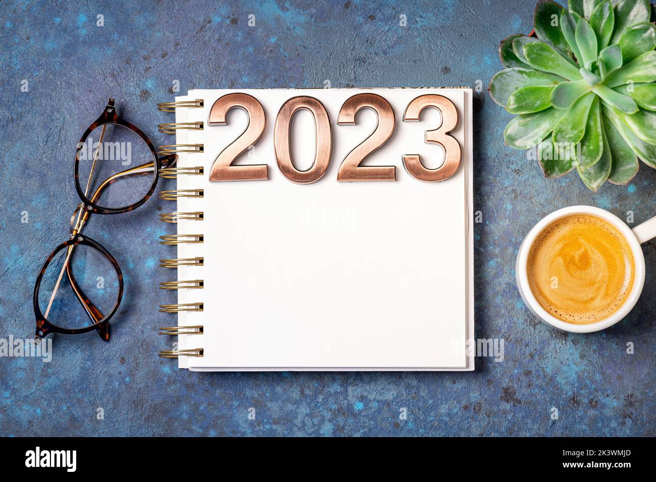 New year goals 2023 on desk. 2023 resolutions list with notebook, coffee cup and Cristmas tree on blue table. Resolutions, plan, goals, action, checkl Stock Photo