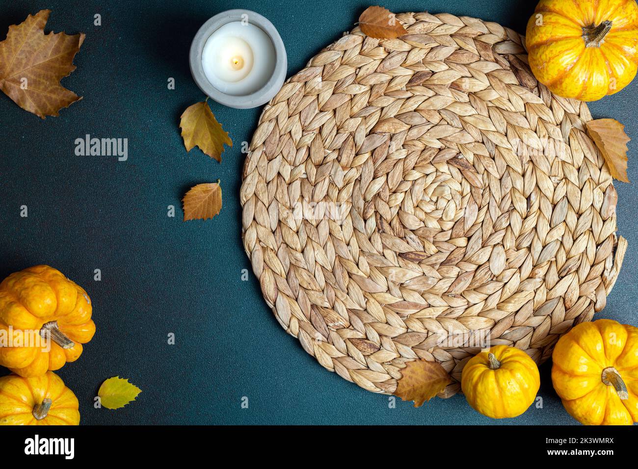 Holiday Thanksgiving table setting background. Top view of wicker place mat, pumpkins, autumn leaves, candle on dark table. Autumn table setting. Rest Stock Photo