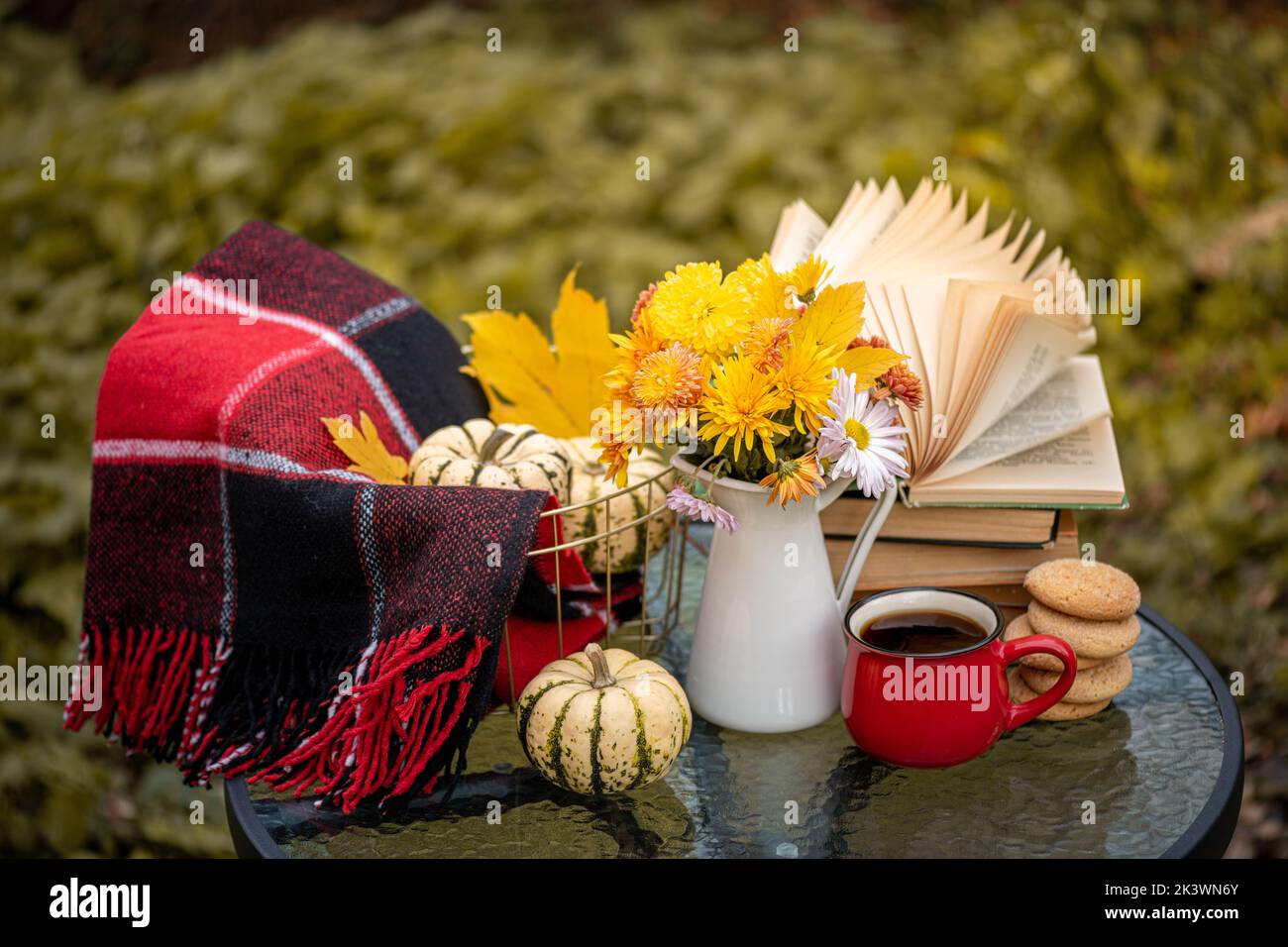 Bouquet of flowers, pumpkin, coffee cup, books on table in autumn garden. Rest in garden, reading books, breakfast, cozy in nature concept. Autumn tim Stock Photo