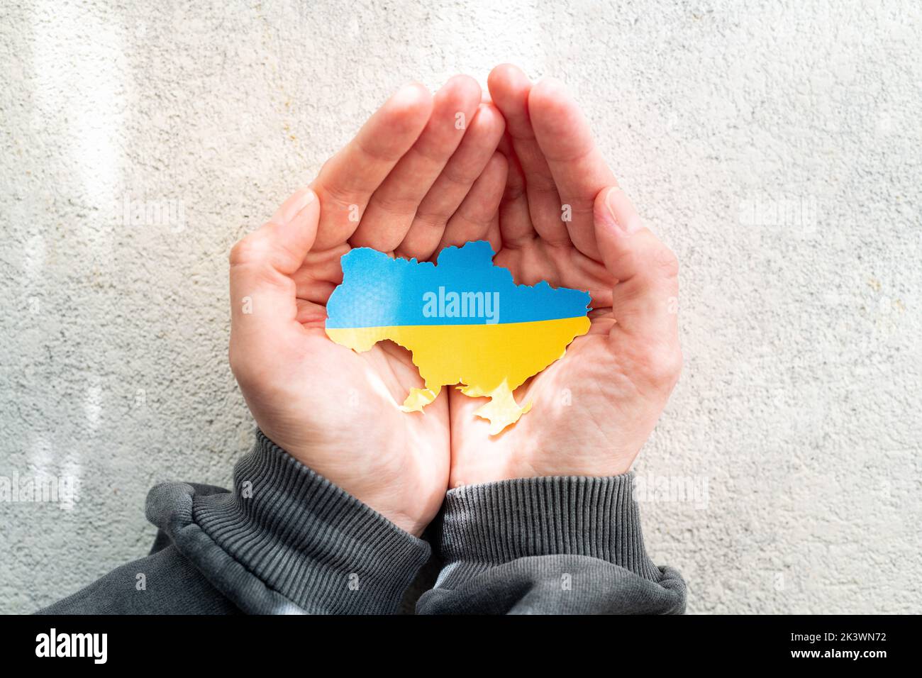 Hands holding the national flag of Ukraine in the shape of the borders of Ukraine. Support for Ukraine in the war with Russia. Stop the war concept Stock Photo