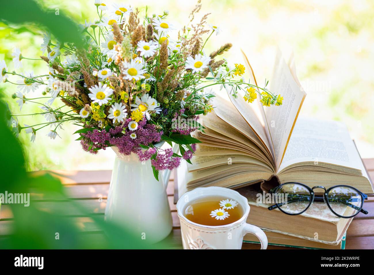 Bouquet of meadow flowers, croissant, cup of tea or coffee, books on table in summer garden. Rest in garden, reading books, breakfast, vacations in na Stock Photo