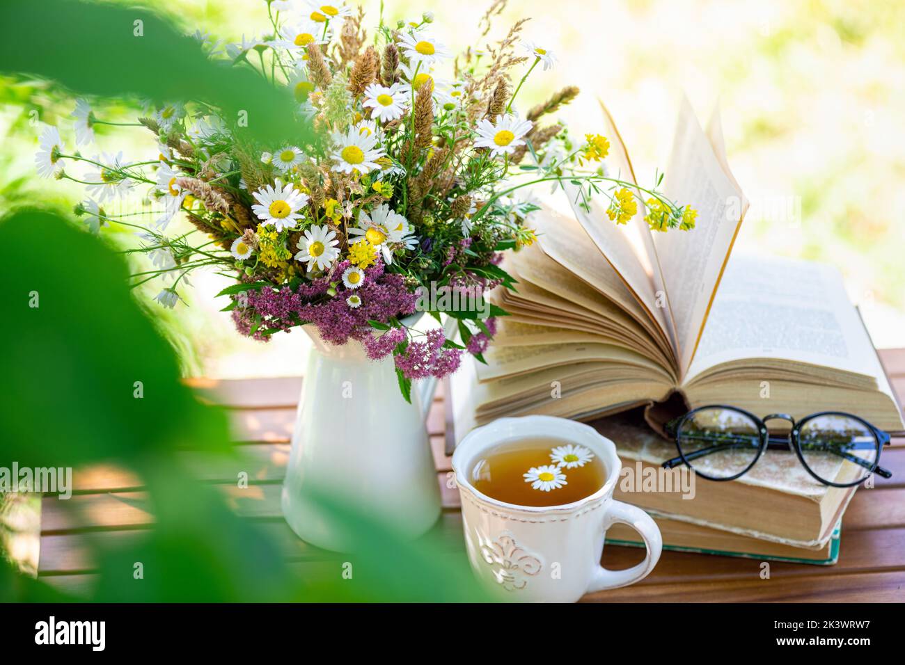 Bouquet of meadow flowers, croissant, cup of tea or coffee, books on table in summer garden. Rest in garden, reading books, breakfast, vacations in na Stock Photo