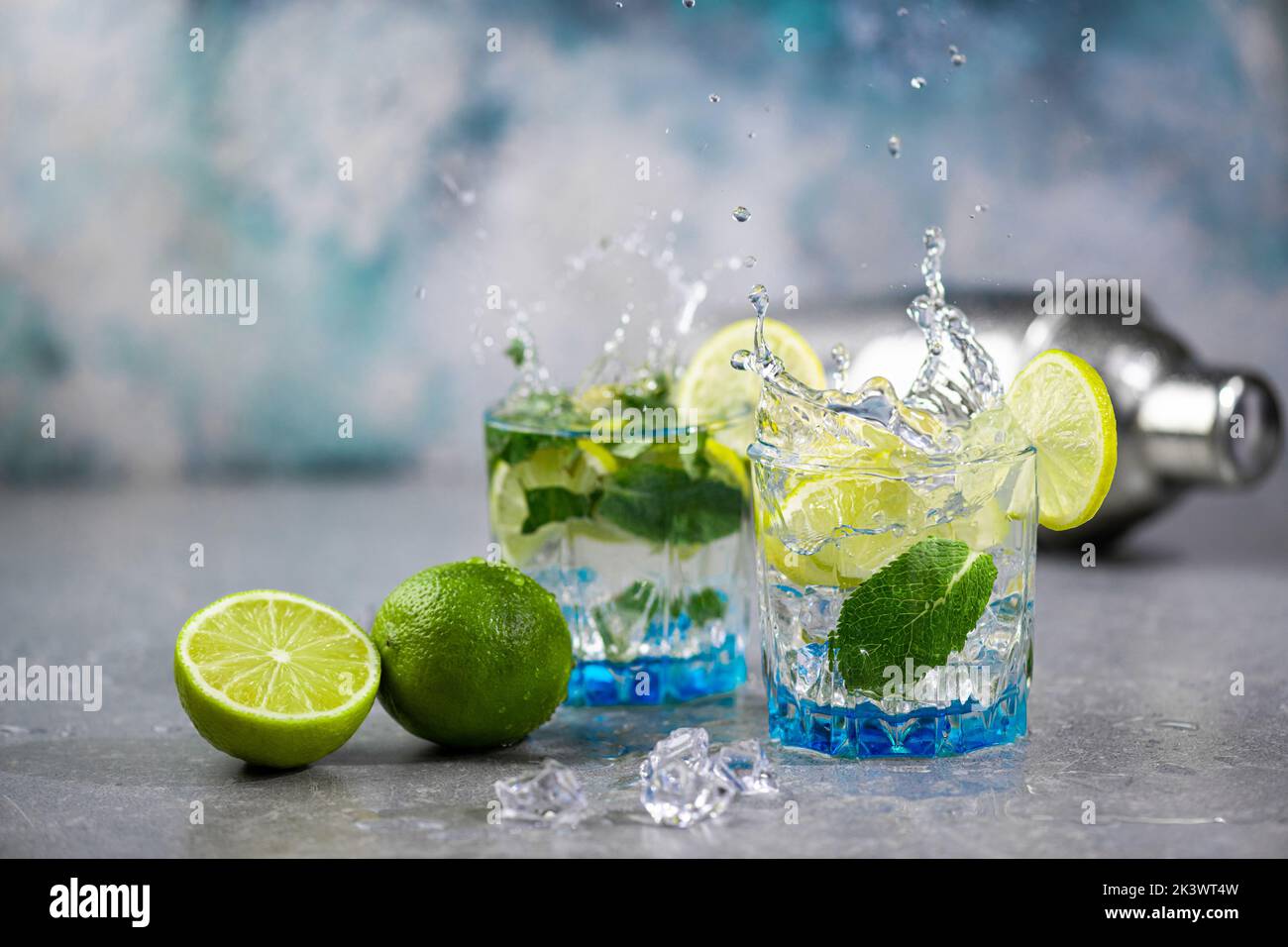 Summer alcoholic cocktail mojito with rum, mint, lime and ice, bar tools on concrete gray blue background. Mojito cocktail with splash and drops Stock Photo