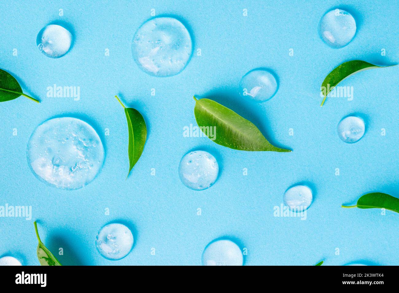 Cosmetics gel and green leaves on blue background. Texture of blue gel or sanitizer. Blue cosmetics gel for face cleansing. Moisturizing, beauty produ Stock Photo
