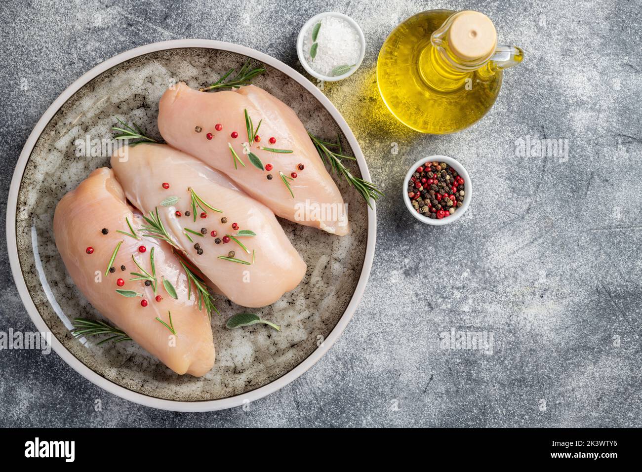 Raw uncooked chicken breasts on grey concrete background, chicken meat with ingredients for cooking. Copy space, top view Stock Photo