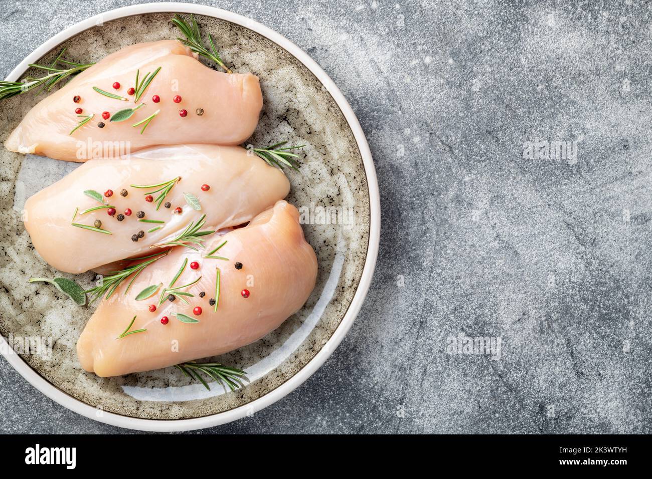 Raw uncooked chicken breasts with spices and herbs on gray concrete table, chicken meat with ingredients for cooking. Top view Stock Photo