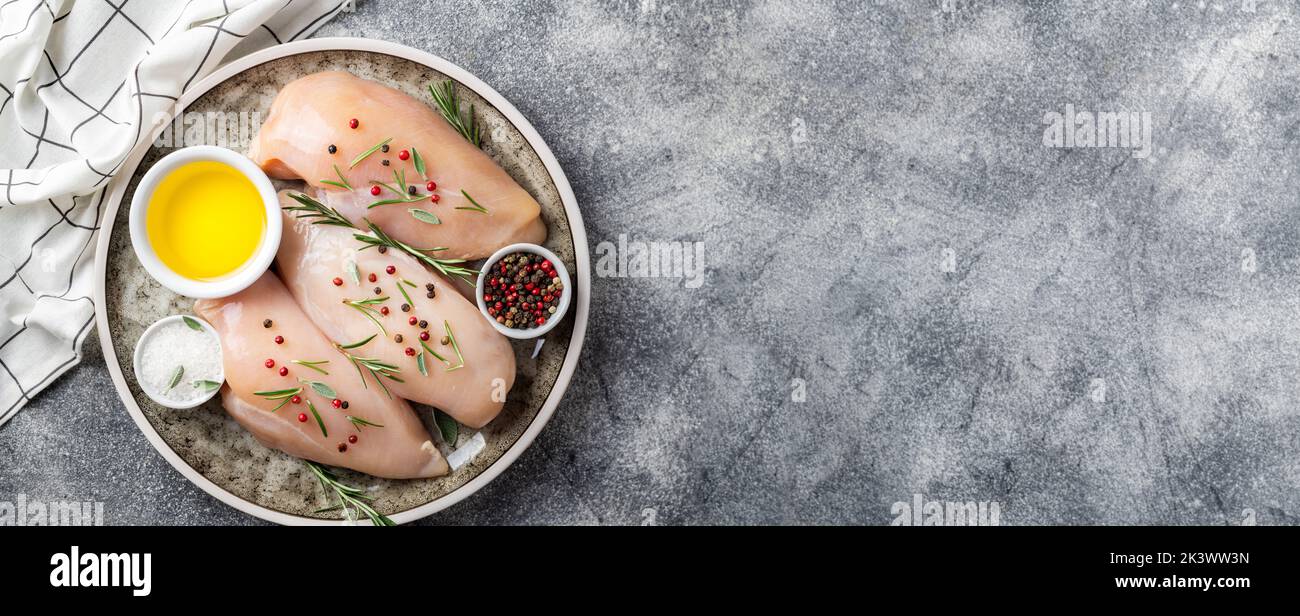 Raw uncooked chicken breasts with spices and herbs on gray concrete table, chicken meat with ingredients for cooking. Top view, copy space Stock Photo
