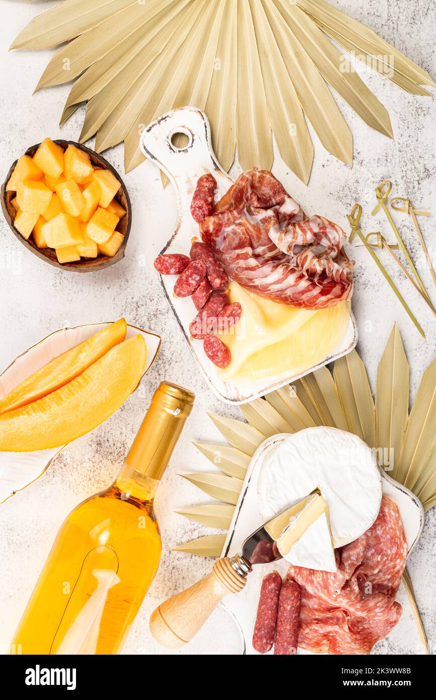 Appetizers on table, antipasto snacks, wine and fruits. Melon cantaloupe, cheese, prosciutto, meat snaks on table decorated palm leaf. Antipasti, gour Stock Photo