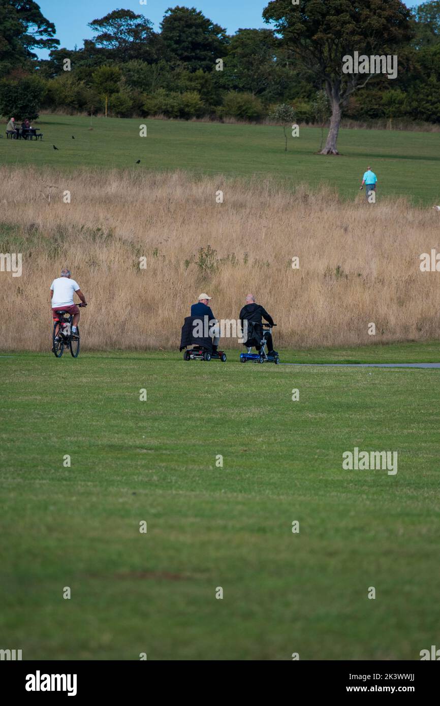 Two senior men on mobility scooters being passed by cyclists on the off
