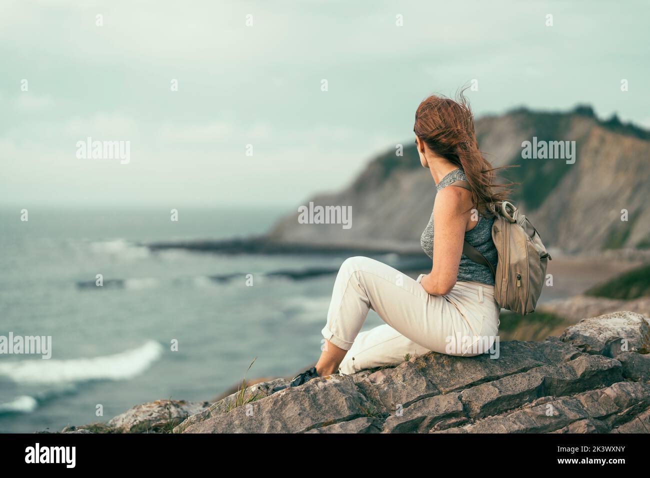 woman sitting on cliff looking towards the beach Stock Photo Alamy