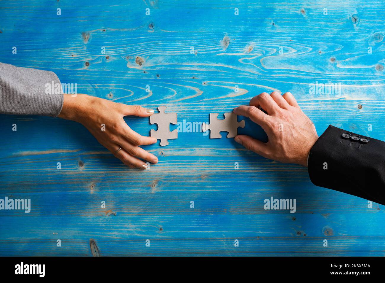 Hands of businesswoman and businessman holding matching puzzle pieces in a conceptual image of problem solving and partnership. Over textured blue woo Stock Photo