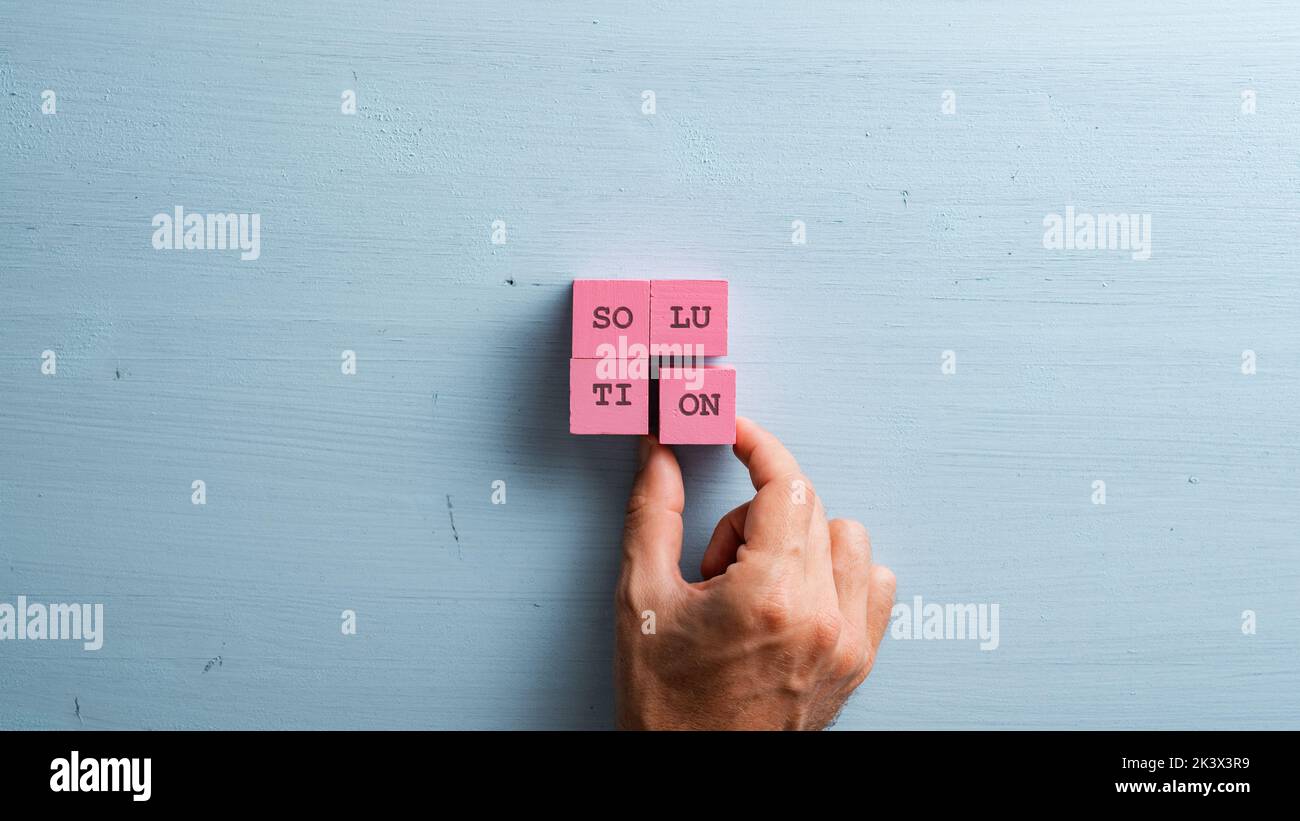 Male hand placing four pink wooden blocks into a square shape to assemble the word Solution. Over pastel blue background. Stock Photo