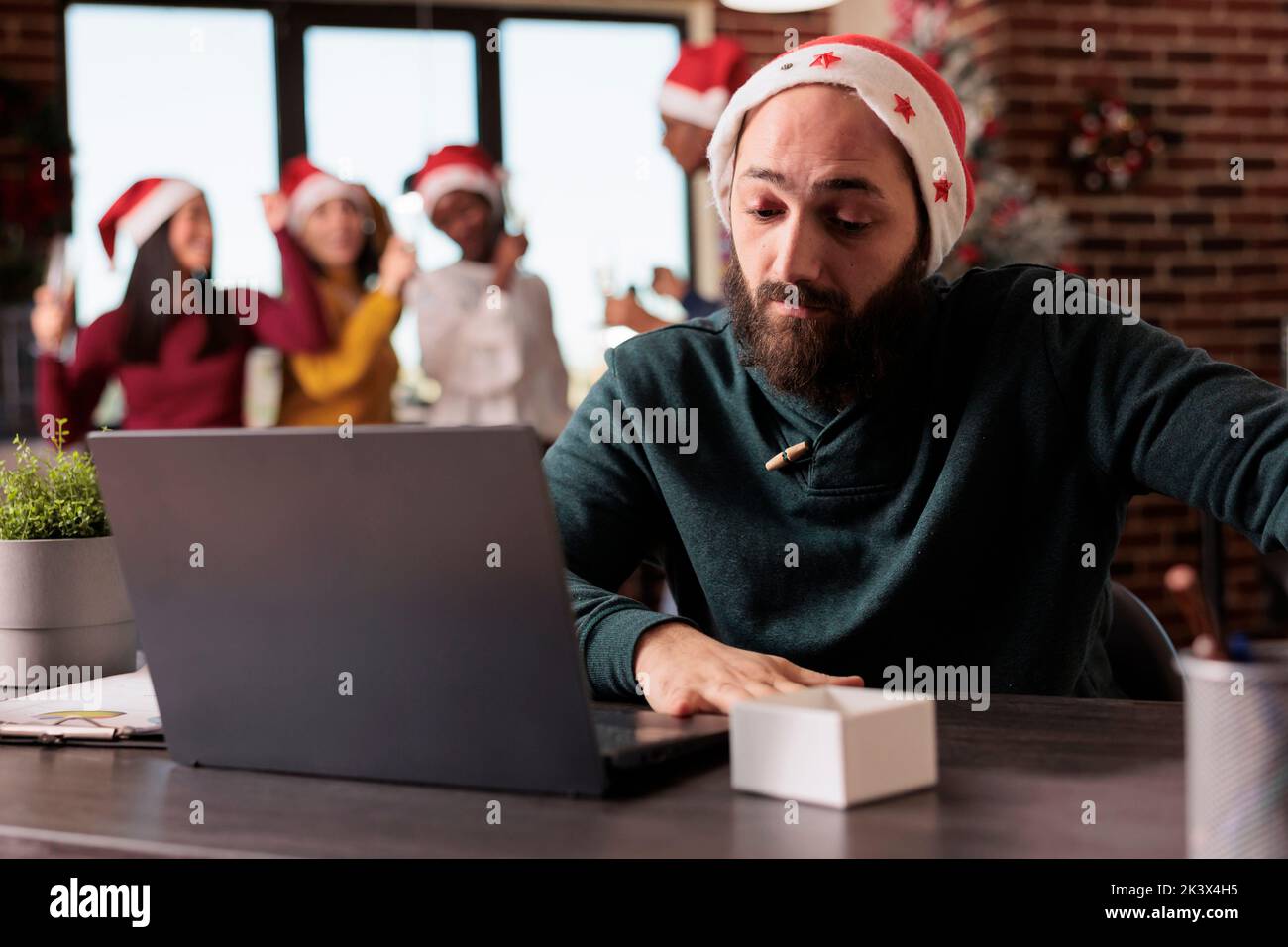 Company worker feeling disturbed at office job because of noisy coworkers celebrating christmas eve. Tired irritated employee being overwhelmed and working during winter holiday season. Stock Photo