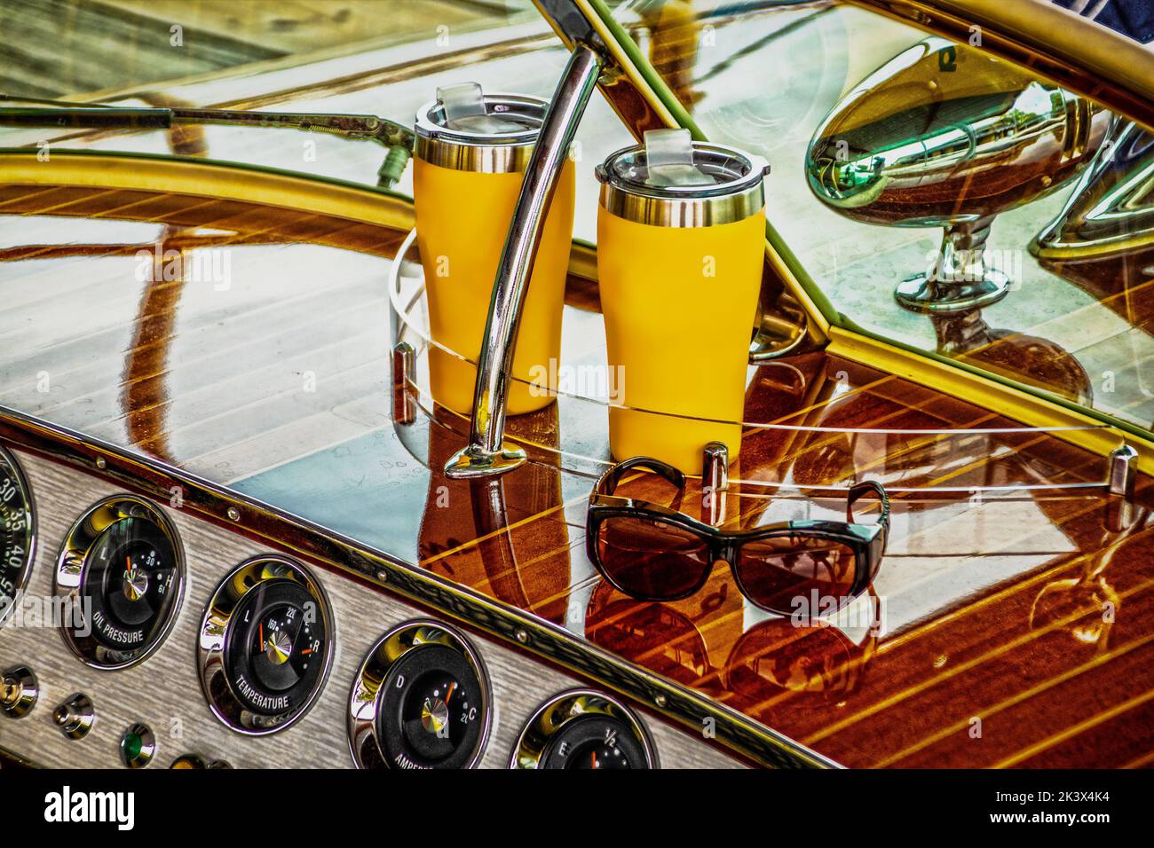 Dash of antique classic wooden speedboat holding two insulated drink cups and sunglasses and gauges below - very shinny with reflections on wood and w Stock Photo
