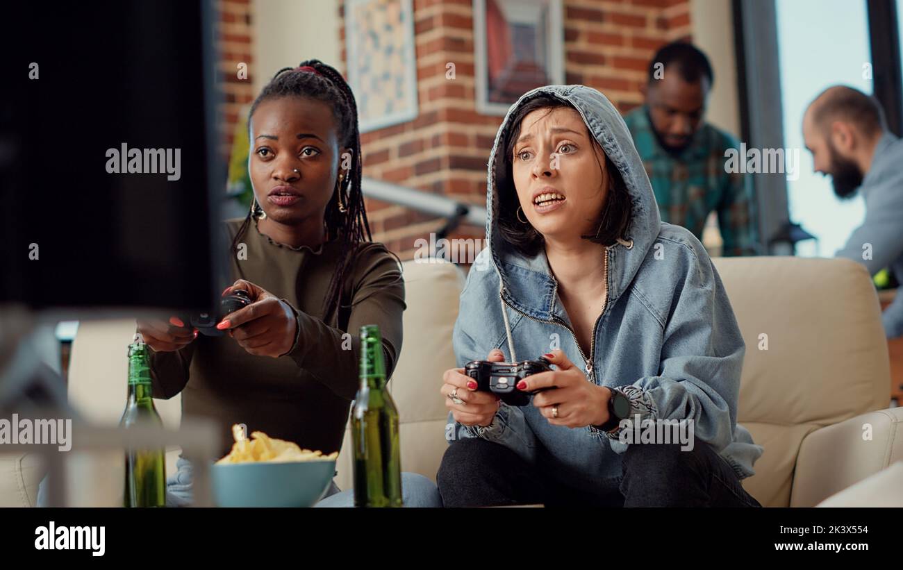 Excited group of friends celebrating video games win, feeling happy about winning online competition with tv gaming console. Cheerful women playing challenge on television. Handheld shot. Stock Photo