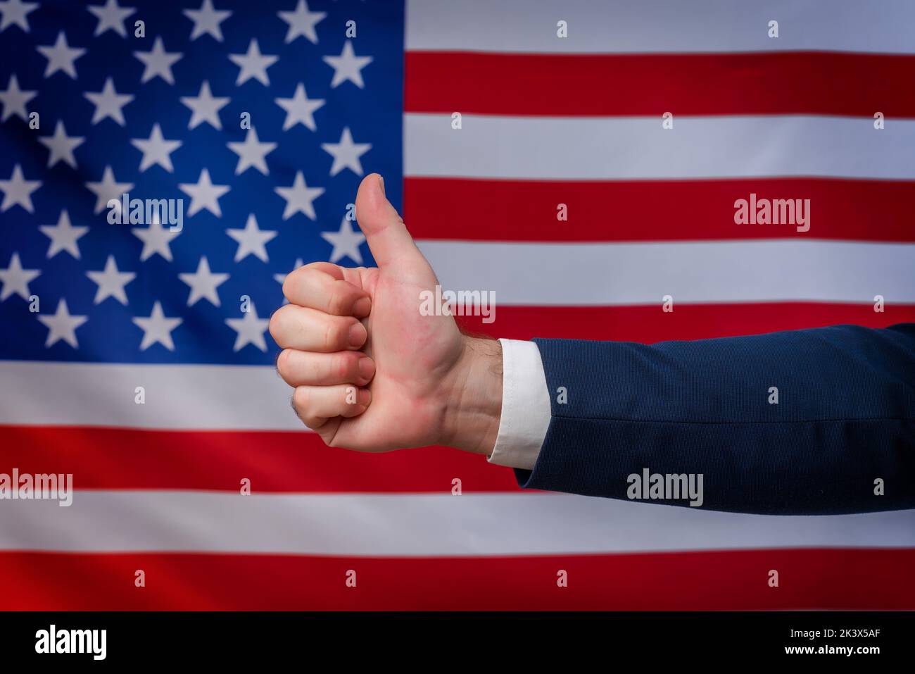 Thumbs up hand in approval with the United States flag in the background. Support for American politics and the American way of life. Vote for America Stock Photo