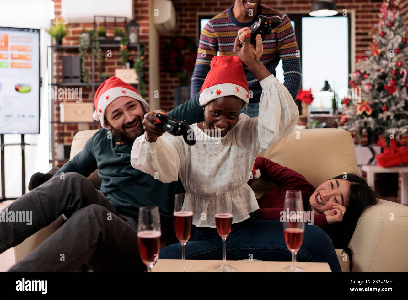 Diverse people enjoying video games play on xmas eve at office party event, celebrating christmas day with gaming competition and alcohol. Colleagues having fun with console on winter holiday. Stock Photo