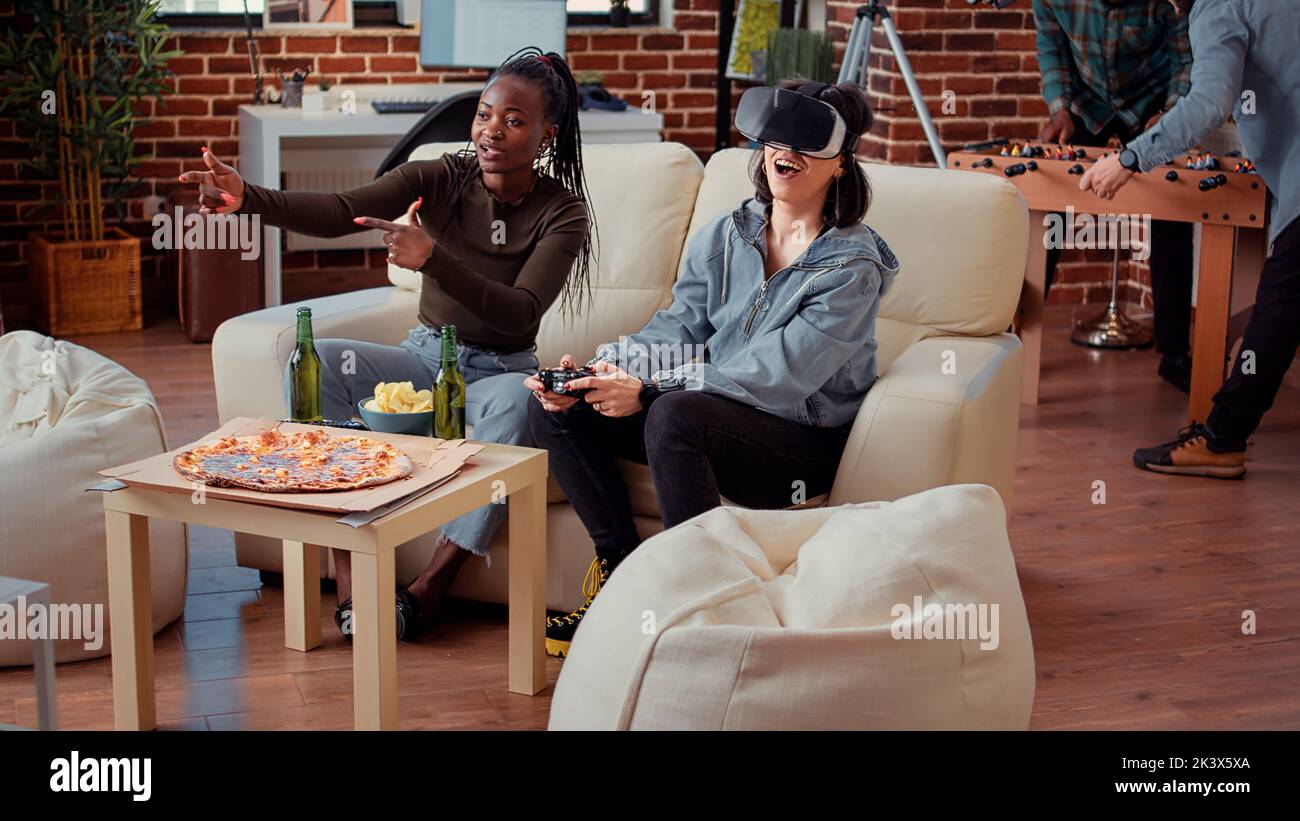 Team of women winning video games play with vr glasses, feeling happy and celebrating gaming win on television console. Playful people enjoying gathering and having fun together. Stock Photo