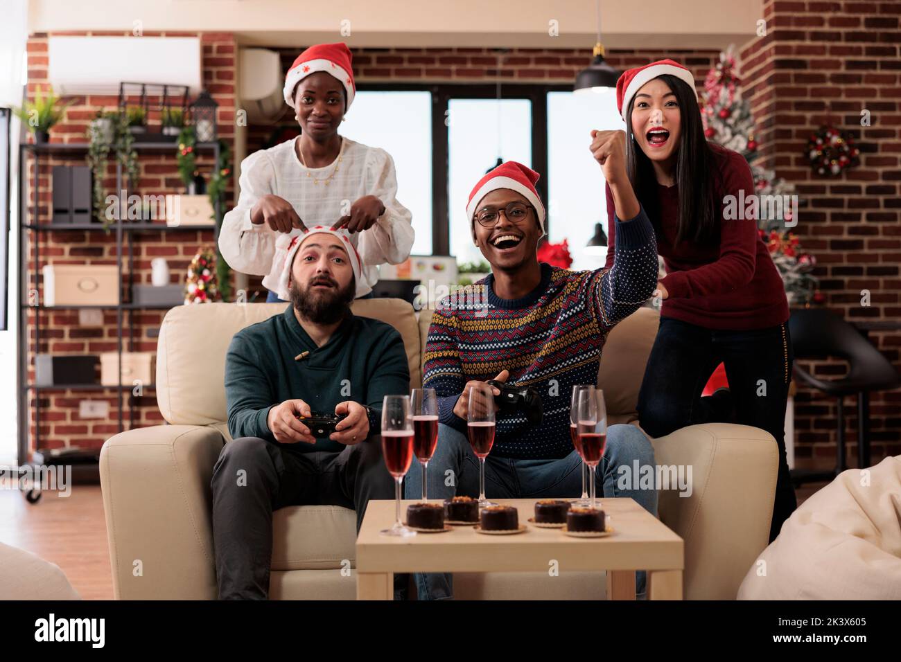 Diverse people playing video games at xmas party event in festive office with christmas tree and ornaments. Having fun with online competition on tv console, celebrating winter holiday. Stock Photo