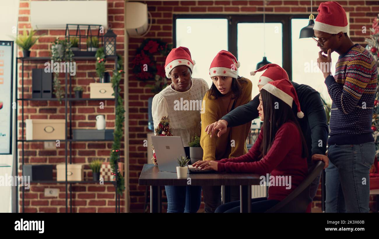 Diverse group of coworkers brainstorming ideas in office with christmas tree and decorations. Doing teamwork to plan report during xmas holiday season in space with festive ornaments. Stock Photo