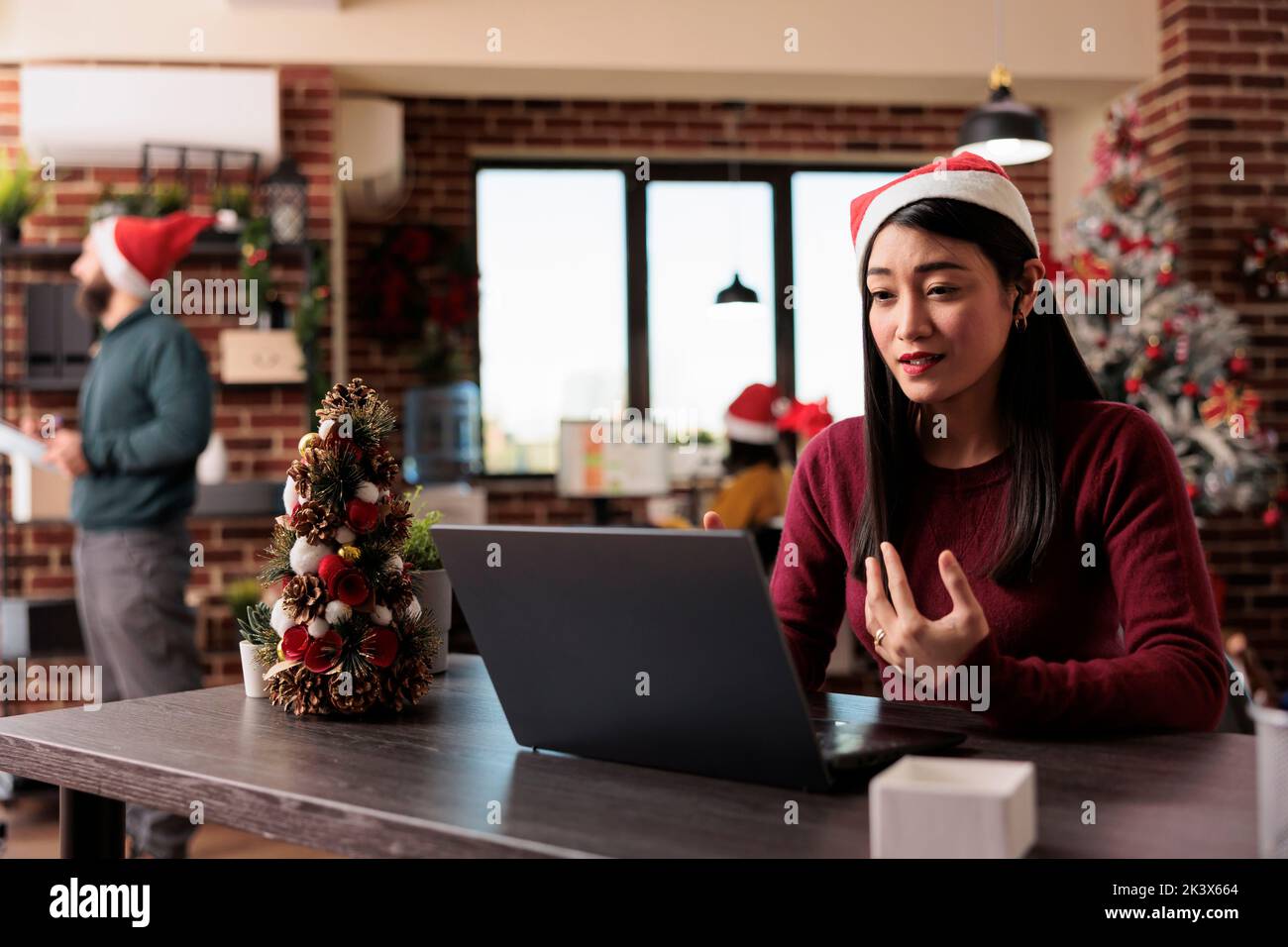 Businesswoman attending videocall meeting in office decorated with christmas tree. Talking on online remote videoconference and teleconference call in workplace with holiday ornaments. Stock Photo